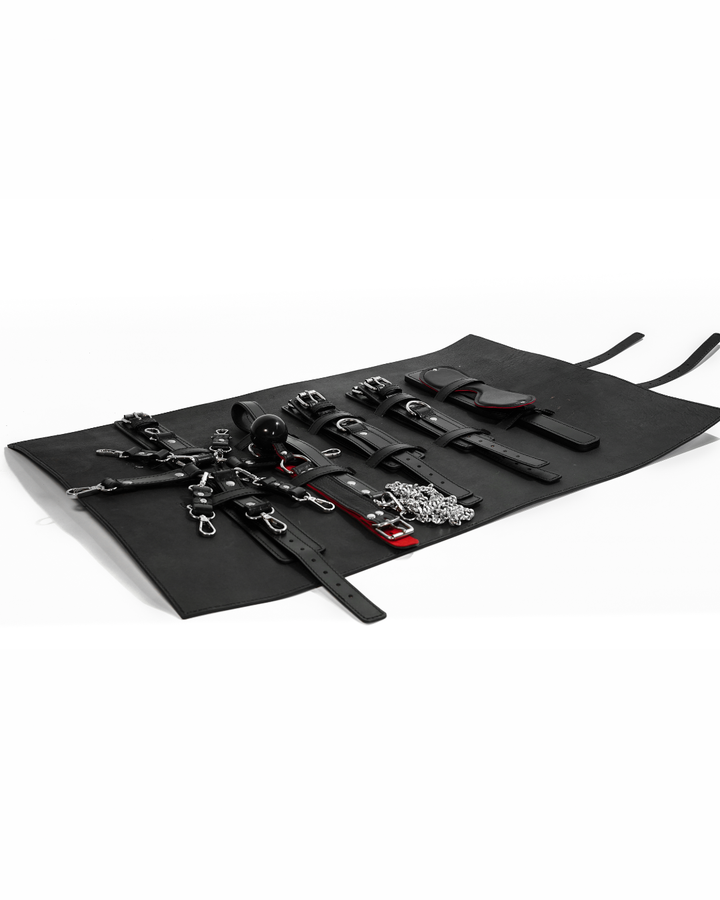 BDSM Bondage Kit flat lay - all five pieces on open leather roll mat: hog-tie set, collar and chain leash, ball gag, paddle and blindfold, Leathersubculture India