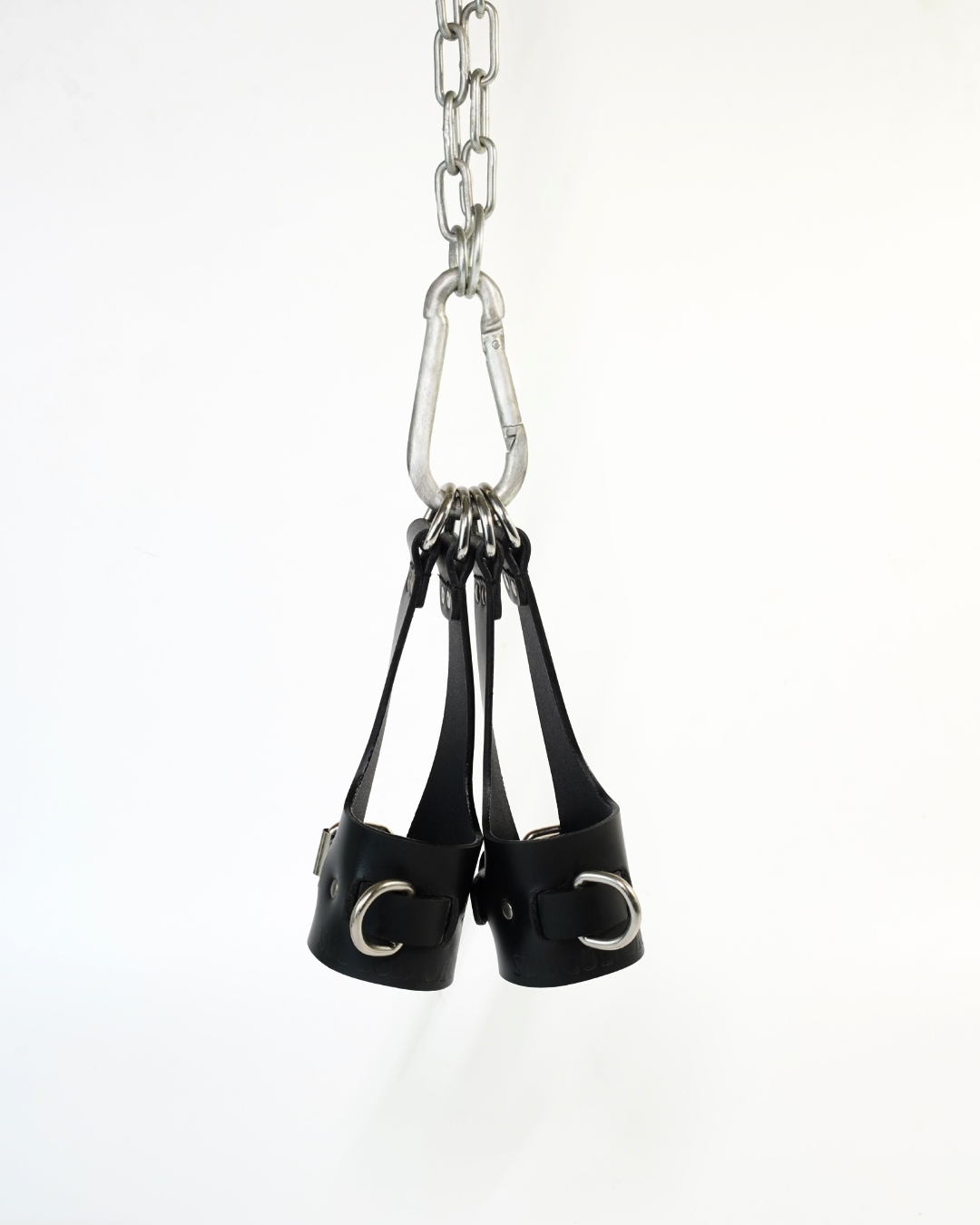 Aloft suspension cuffs hanging from steel carabiner, D-rings gathered at top of leather bridge straps, product shot on white background