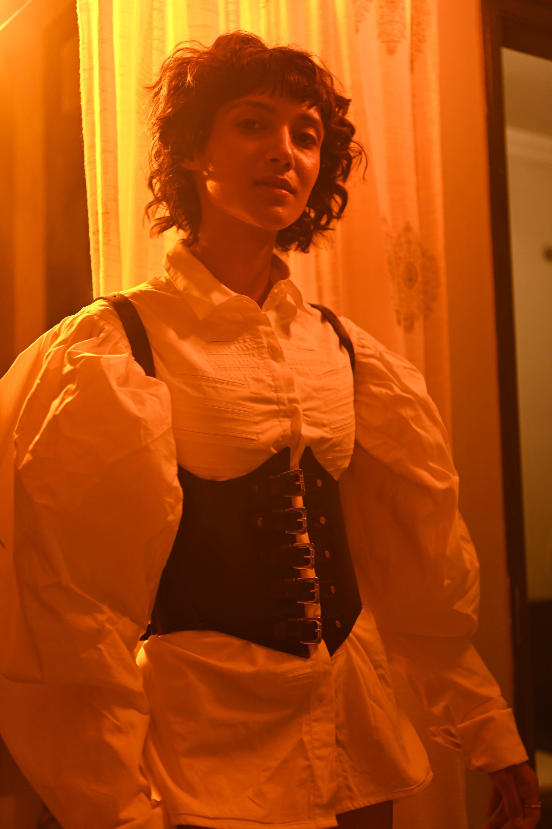 Person wearing a white blouse with a black vest in front of a yellow curtain