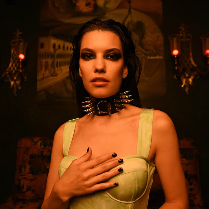 Subculture Rave Collar worn by a female model in a candlelit gothic interior — silver cone spike studs and centre O-ring shown at close range