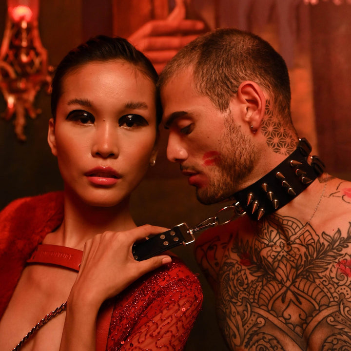 Subculture Rave Collar on a tattooed male model in a red-lit gothic editorial, silver chain leash clipped to the front O-ring