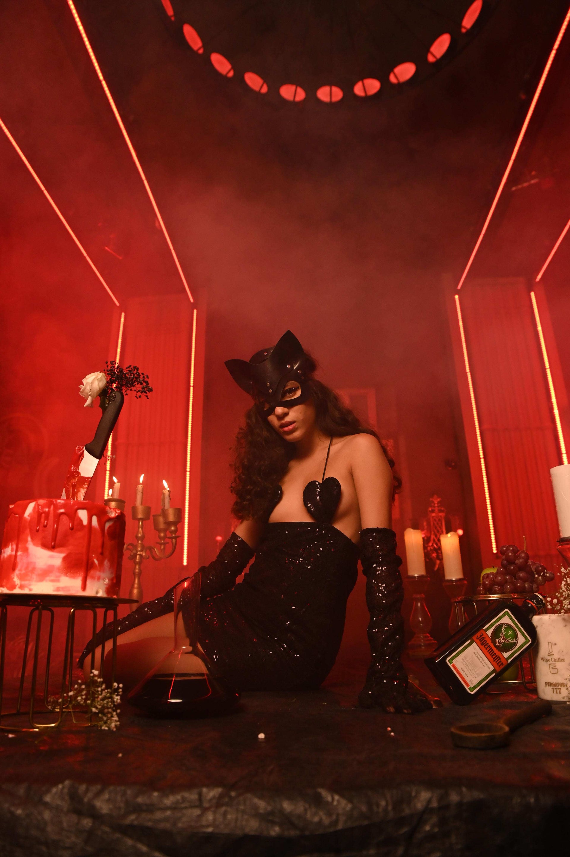 Person in a cat-themed outfit in a red-lit room with candles and decorative items.
