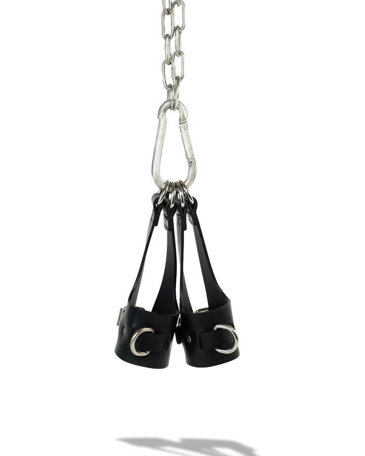 Aloft suspension cuffs hanging from steel carabiner, D-rings gathered at top of leather bridge straps, product shot on white background